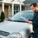 Un homme examine attentivement une voiture d’occasion devant une maison, avec des documents vierges et des clés dans les mains.